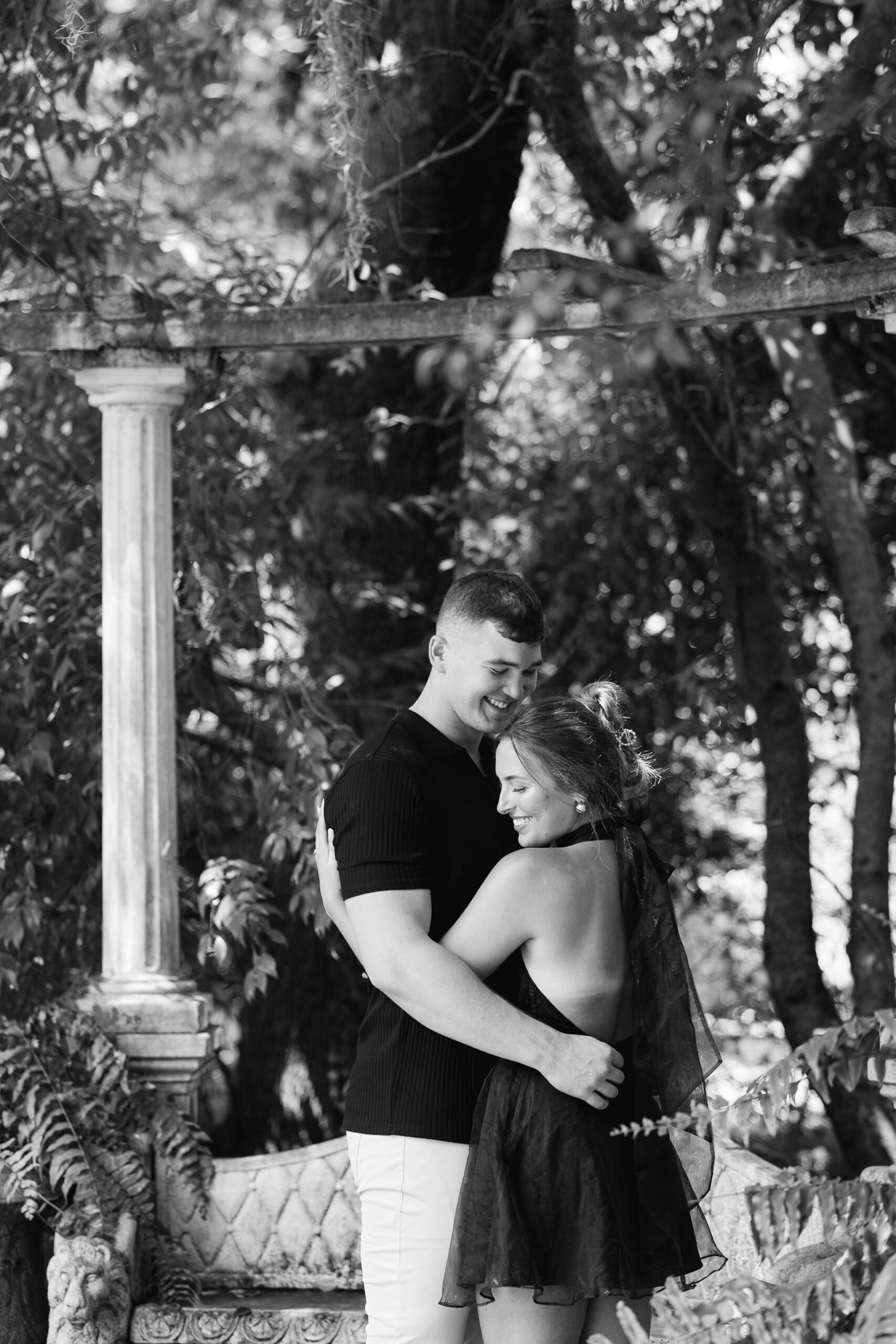 A newly engaged couple giggles while hugging in a garden for their engagement photos Wilmington NC