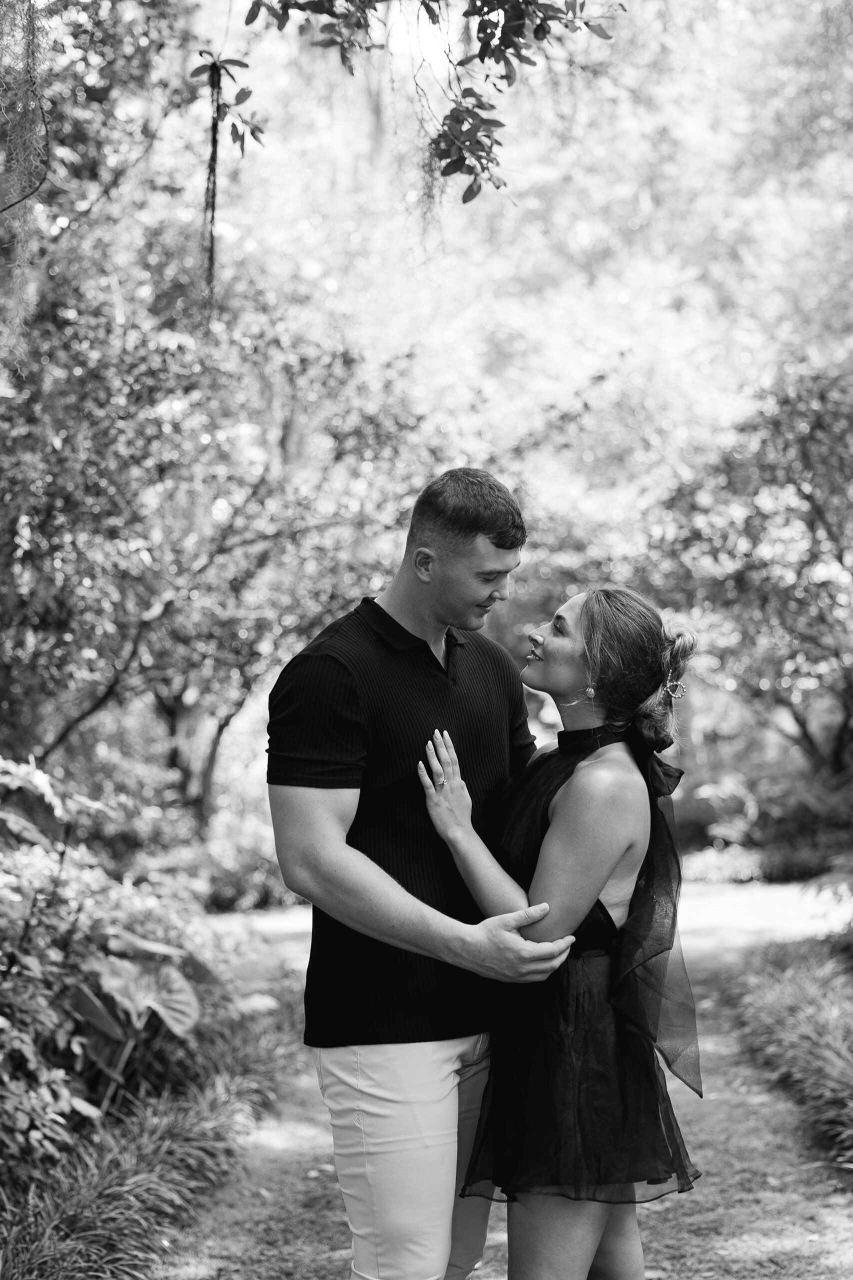 A newly engaged couple stands close in a garden during engagement photos Wilmington NC