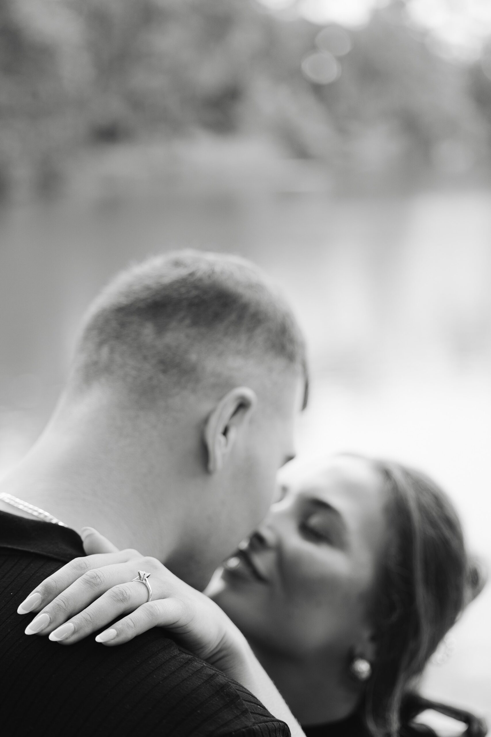 Newly engaged couple kisses on the water while showing off the ring