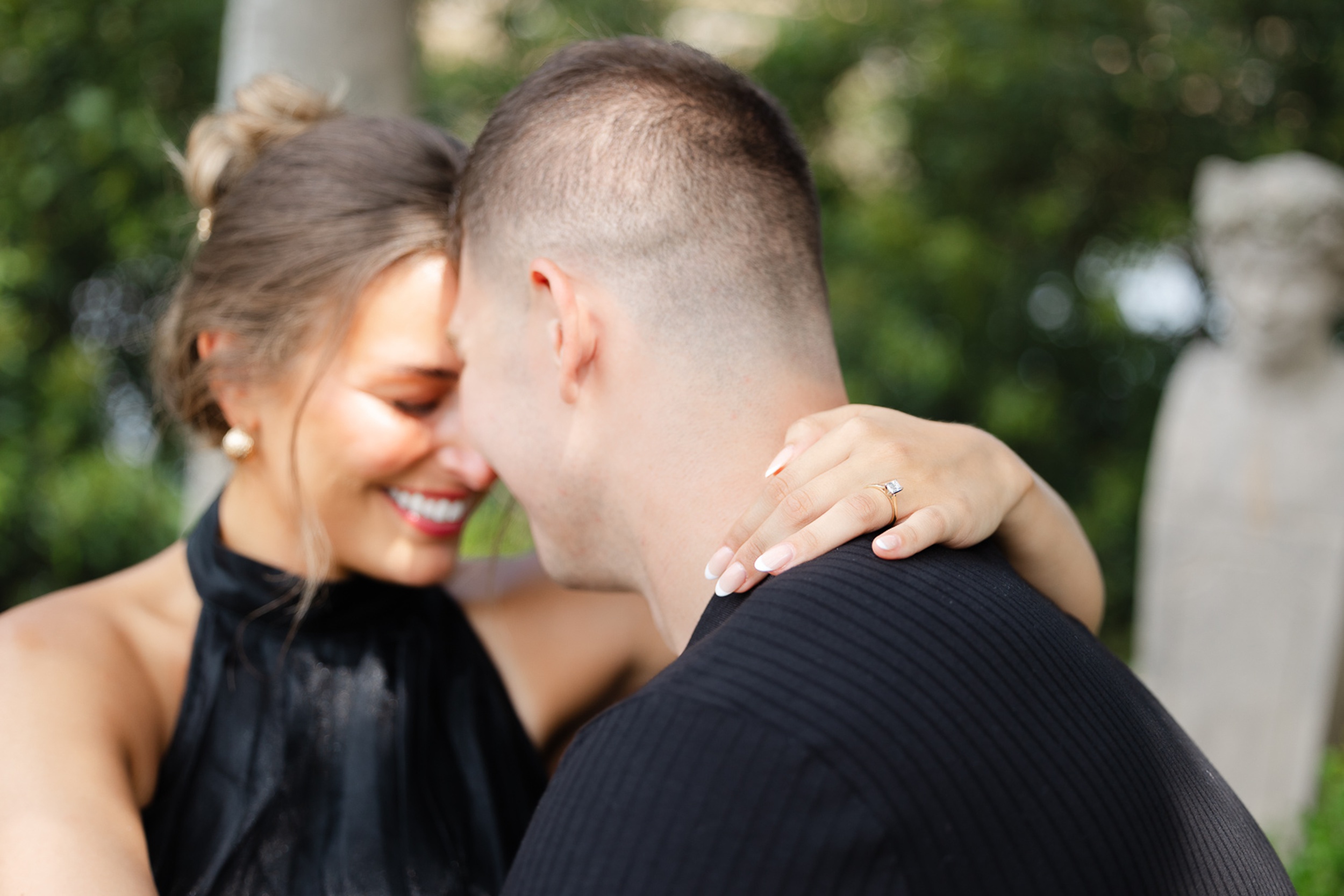 Details of an engagement ring while the couple touches foreheads and giggles