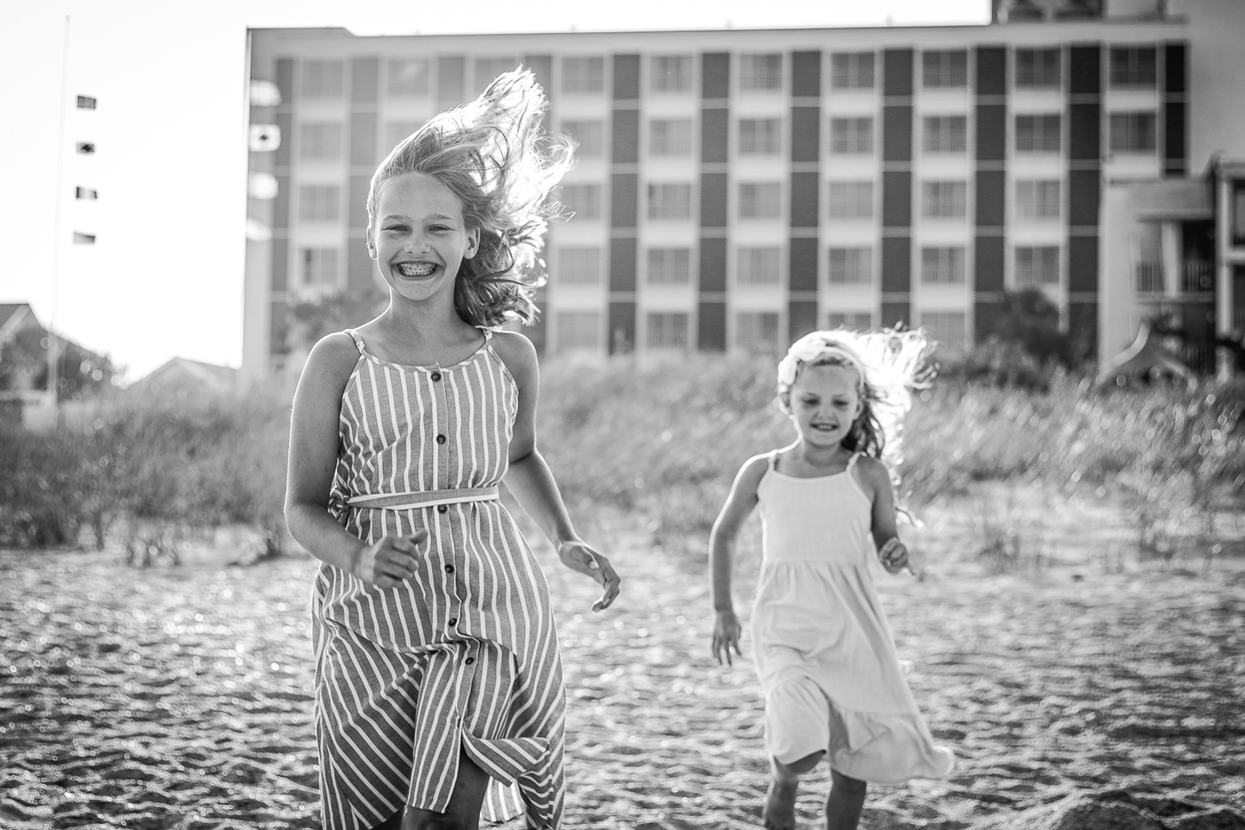 A young girl and her younger sister run on a windy beach during things to do in wilmington with kids