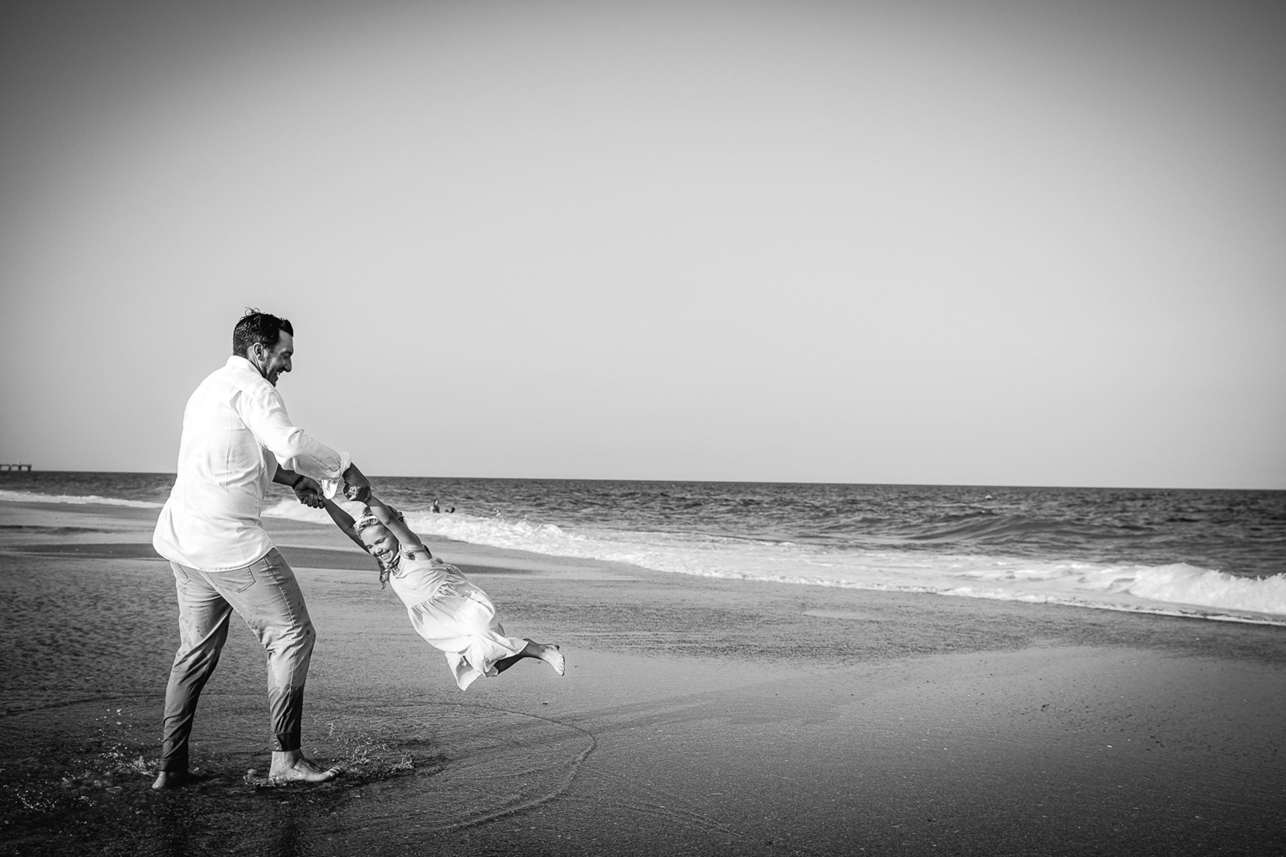 A father holds hands and spins his toddler daughter on a beach during things to do in wilmington with kids