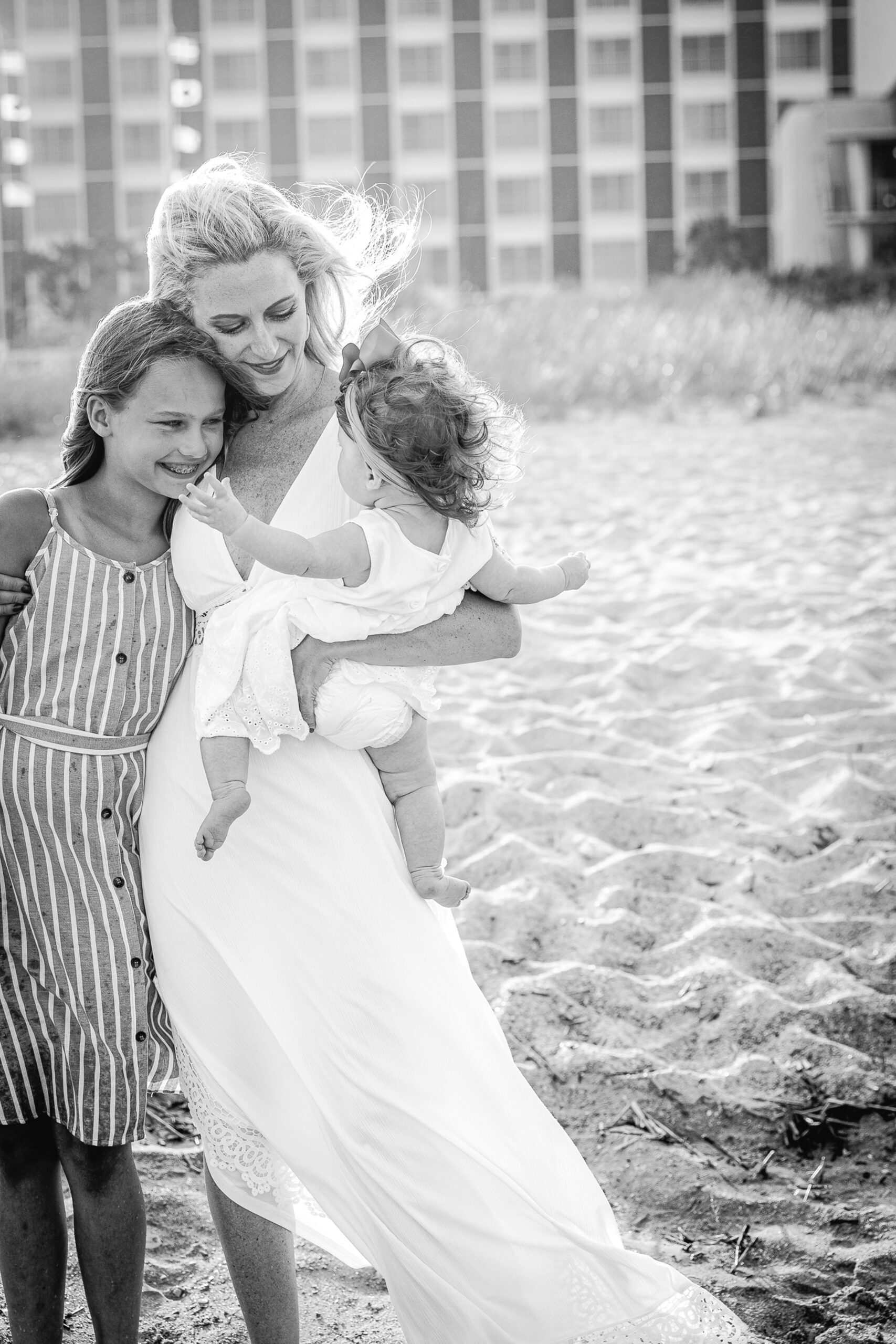 A mother in a long white dress hugs her young daughter while holding her toddler in her other arm during things to do in wilmington with kids