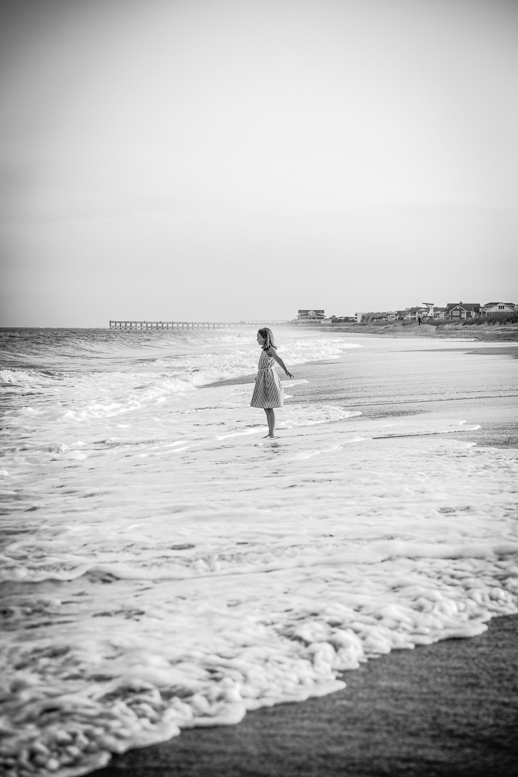 A young girl in a stripe dress plays in the shallow water on the beach