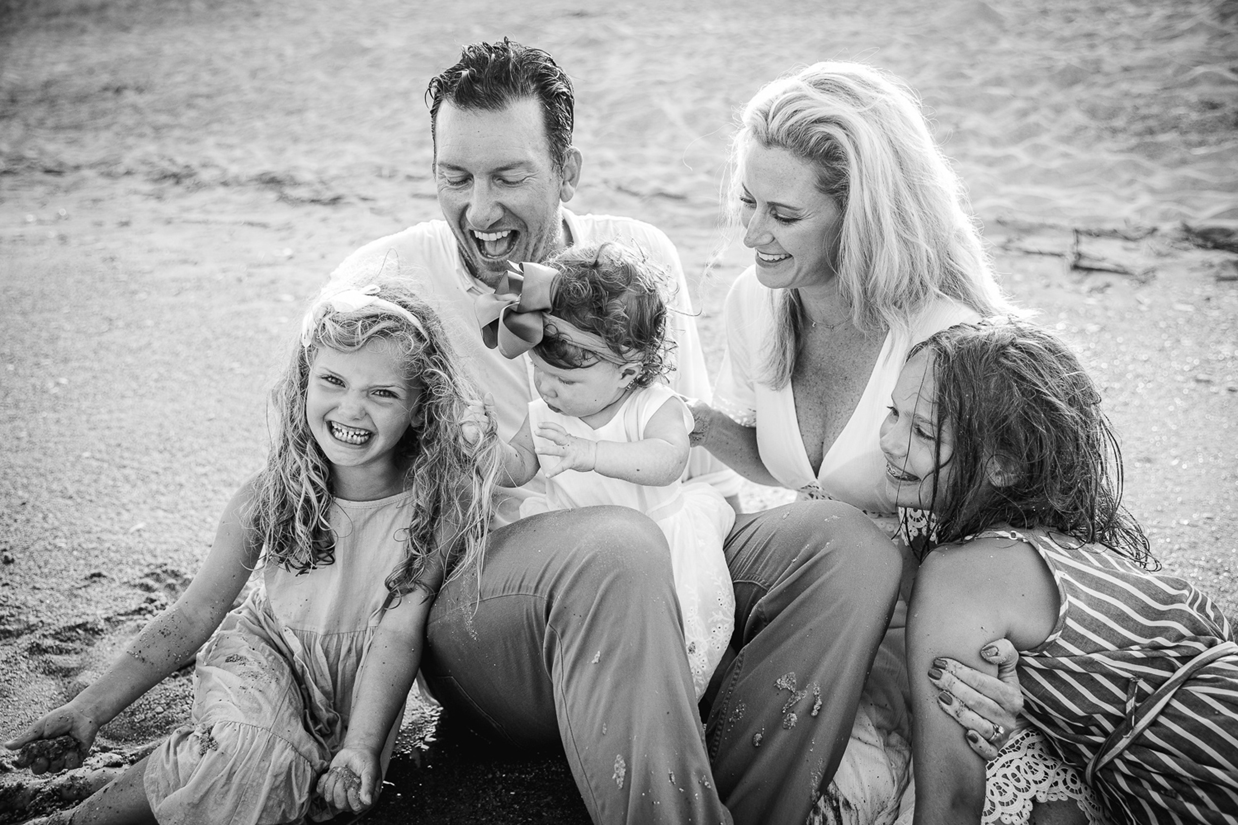 A mom and dad sit on a wet beach while playing with their three young daughters during things to do in wilmington with kids