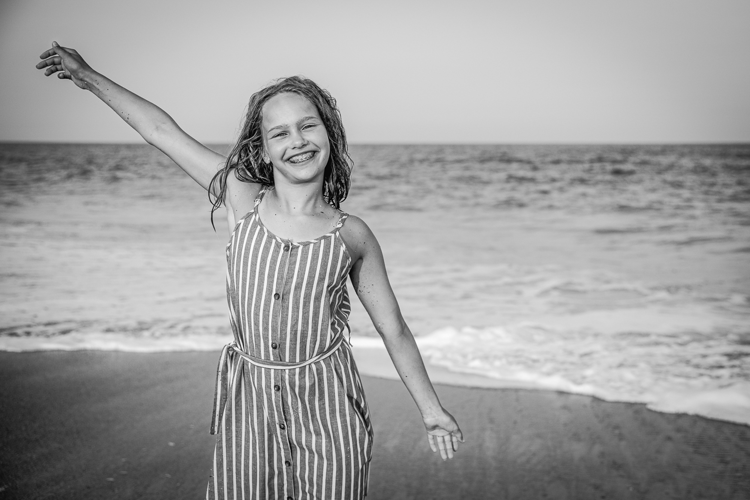 A young girl in a stripe romper laughs and plays on a beach during things to do in wilmington with kids