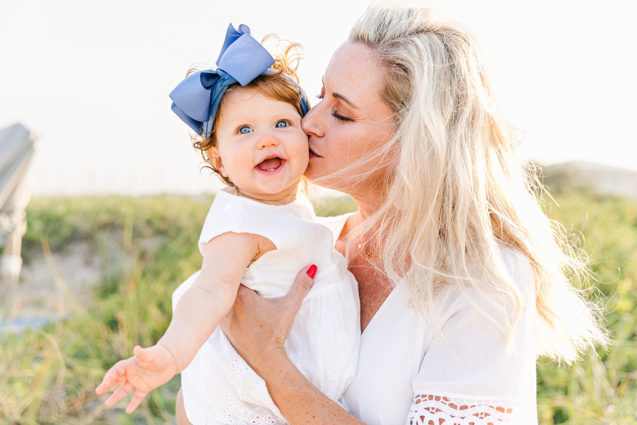 A mother kisses her toddler happy daughter while standing on a beach at sunset