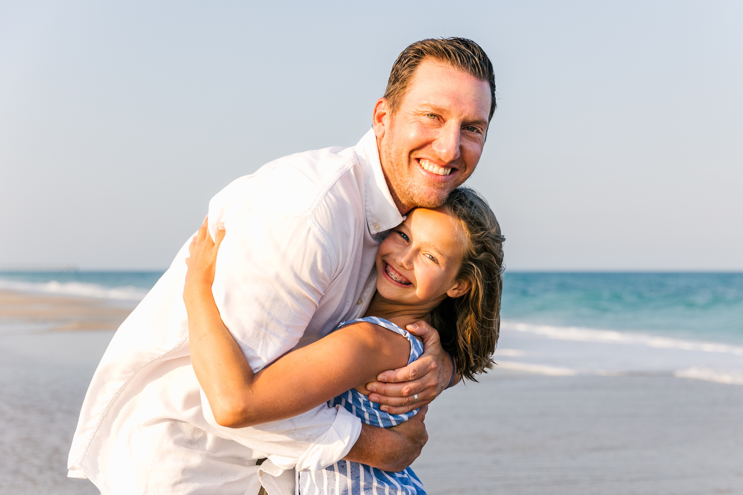 A happy father hugs his young daughter on a beach at sunset