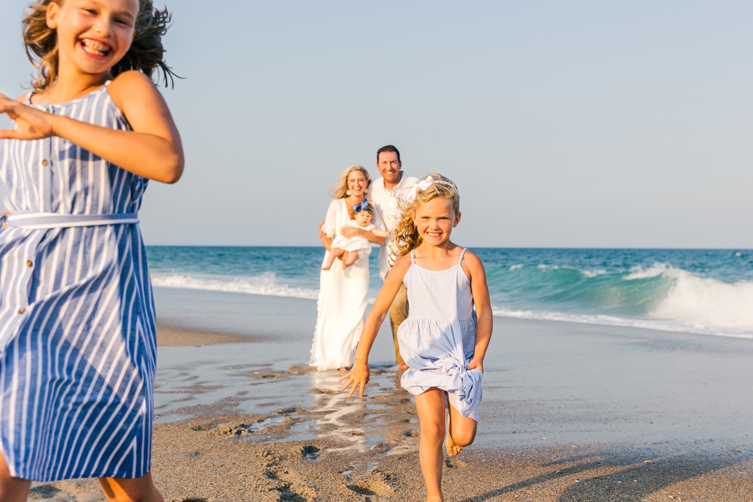 Two young girls run on a beach away from mom and dad during things to do in wilmington with kids