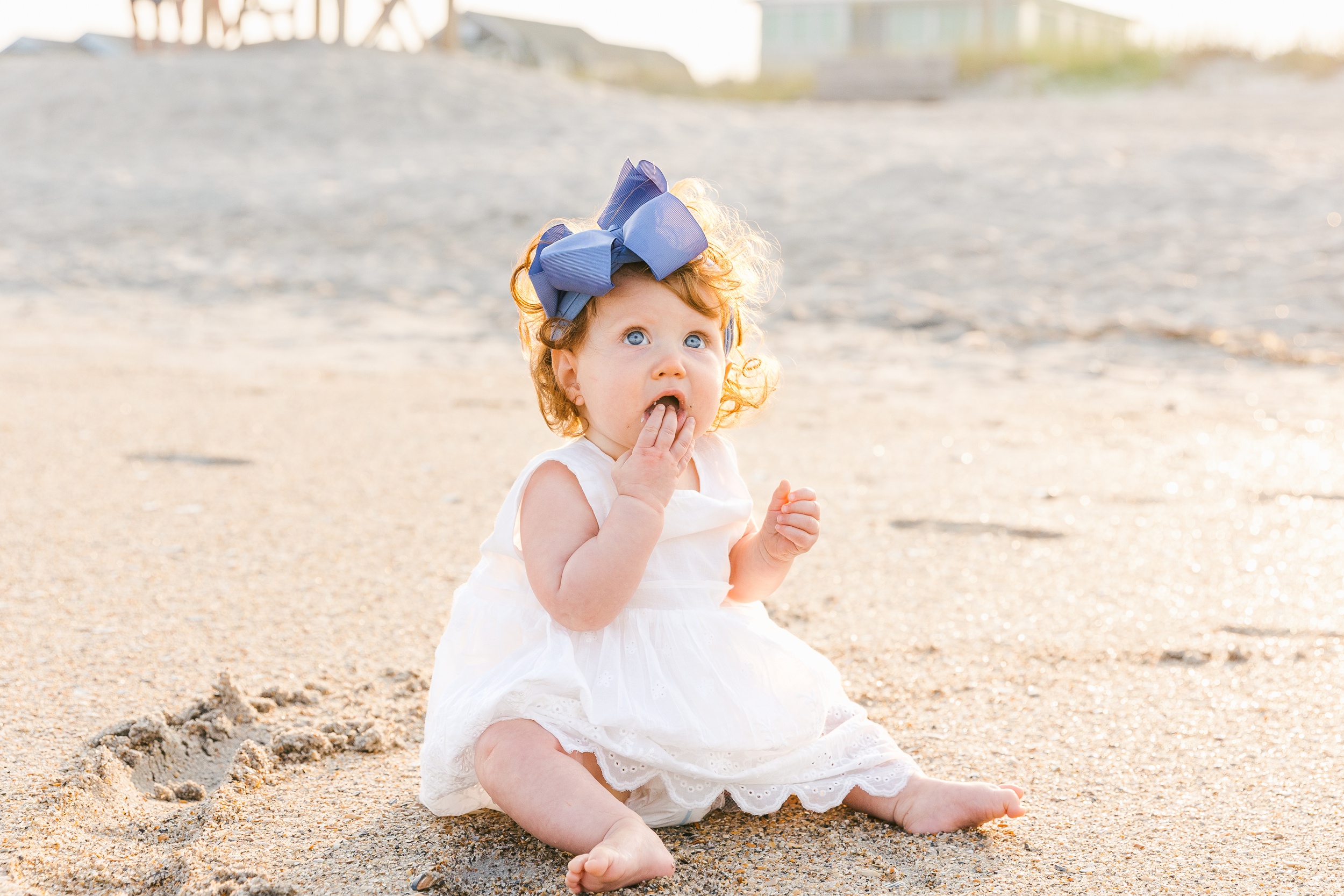 A young toddler girl in a white dress plays in the sand on the beach at sunset while doing things to do in wilmington with kids