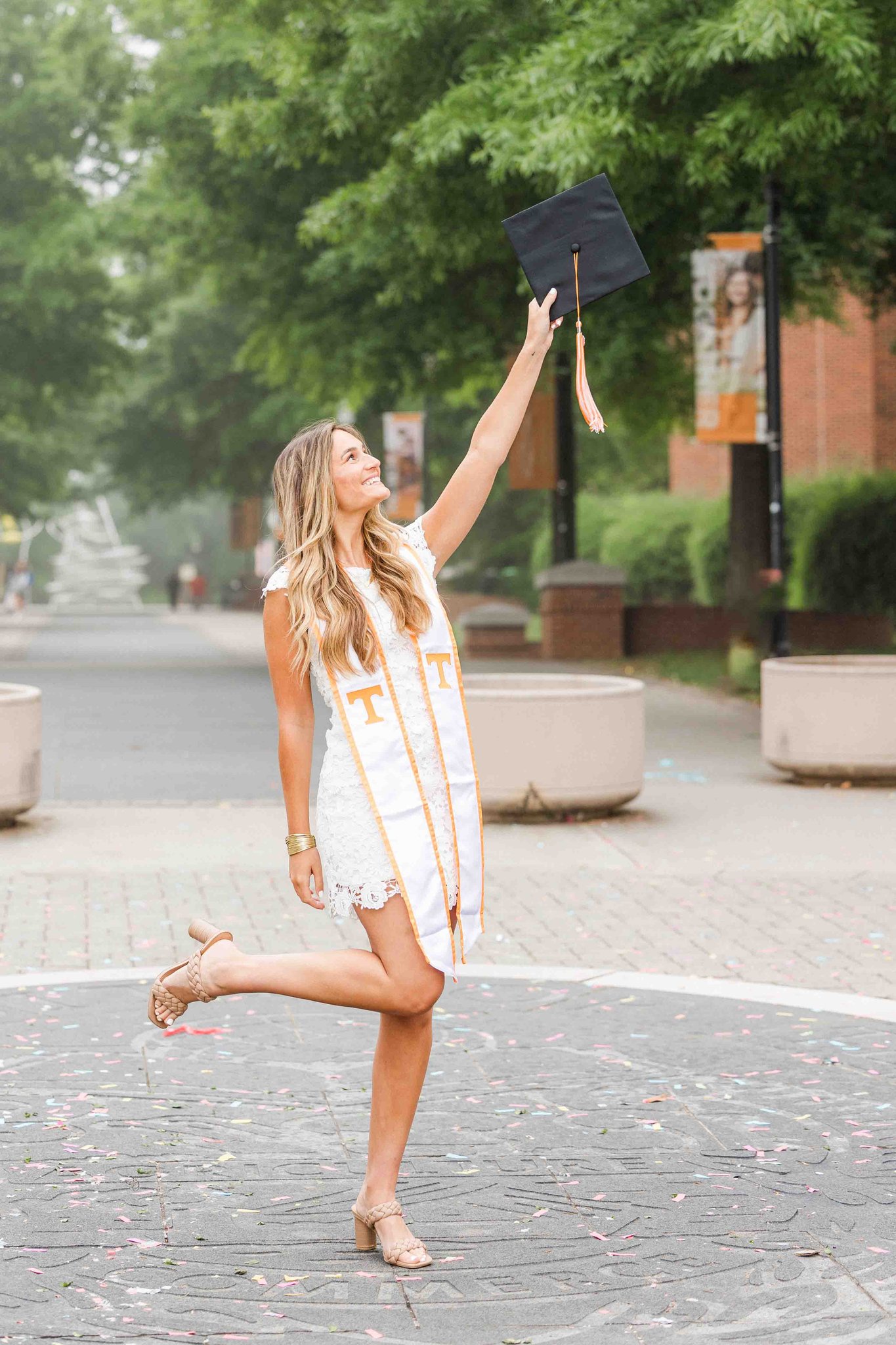 A woman raises her cap in the air while wearing a white dress for her utk graduation pictures