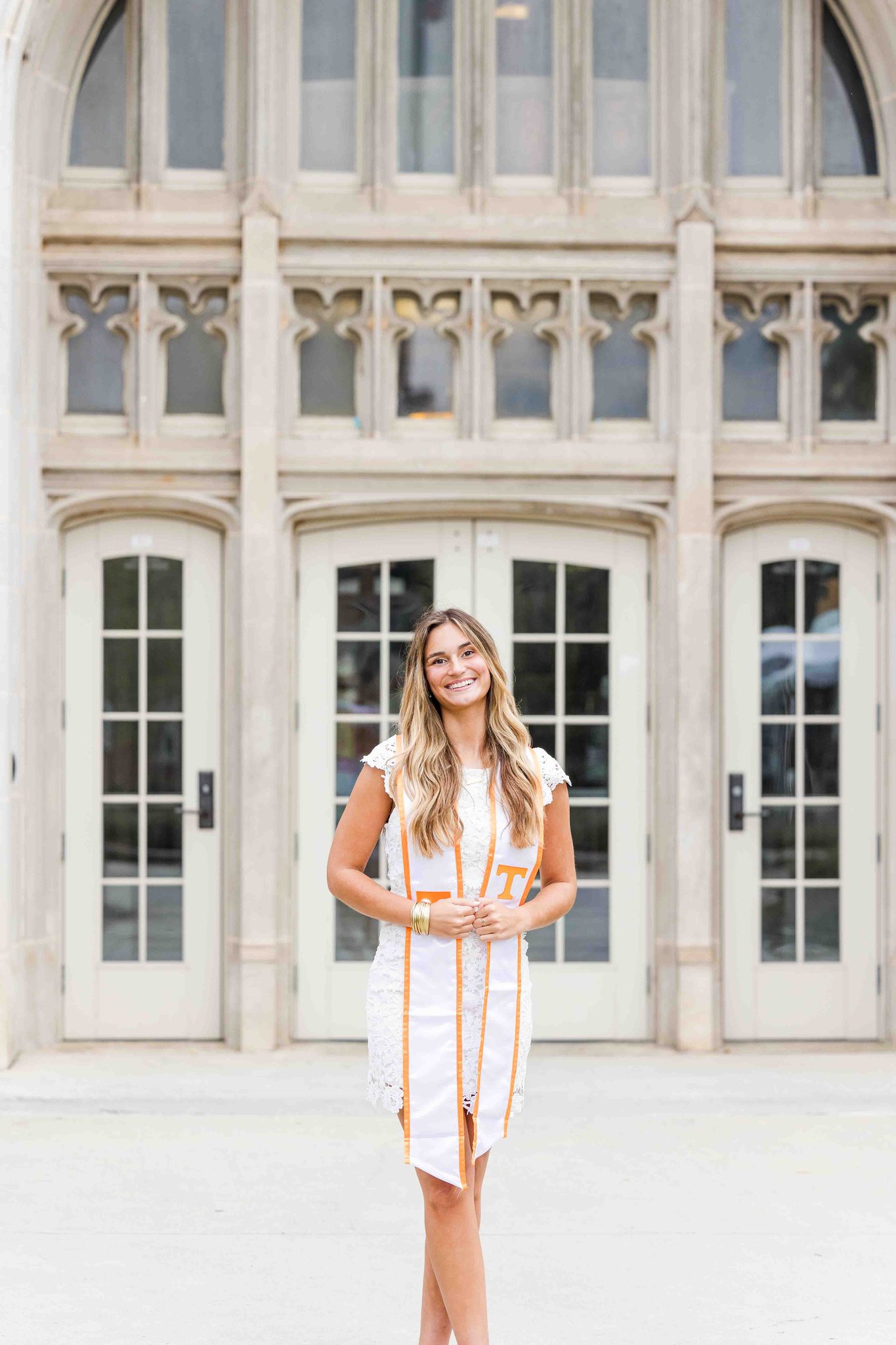 A woman smiles big while wearing a white lace dress and UT stole