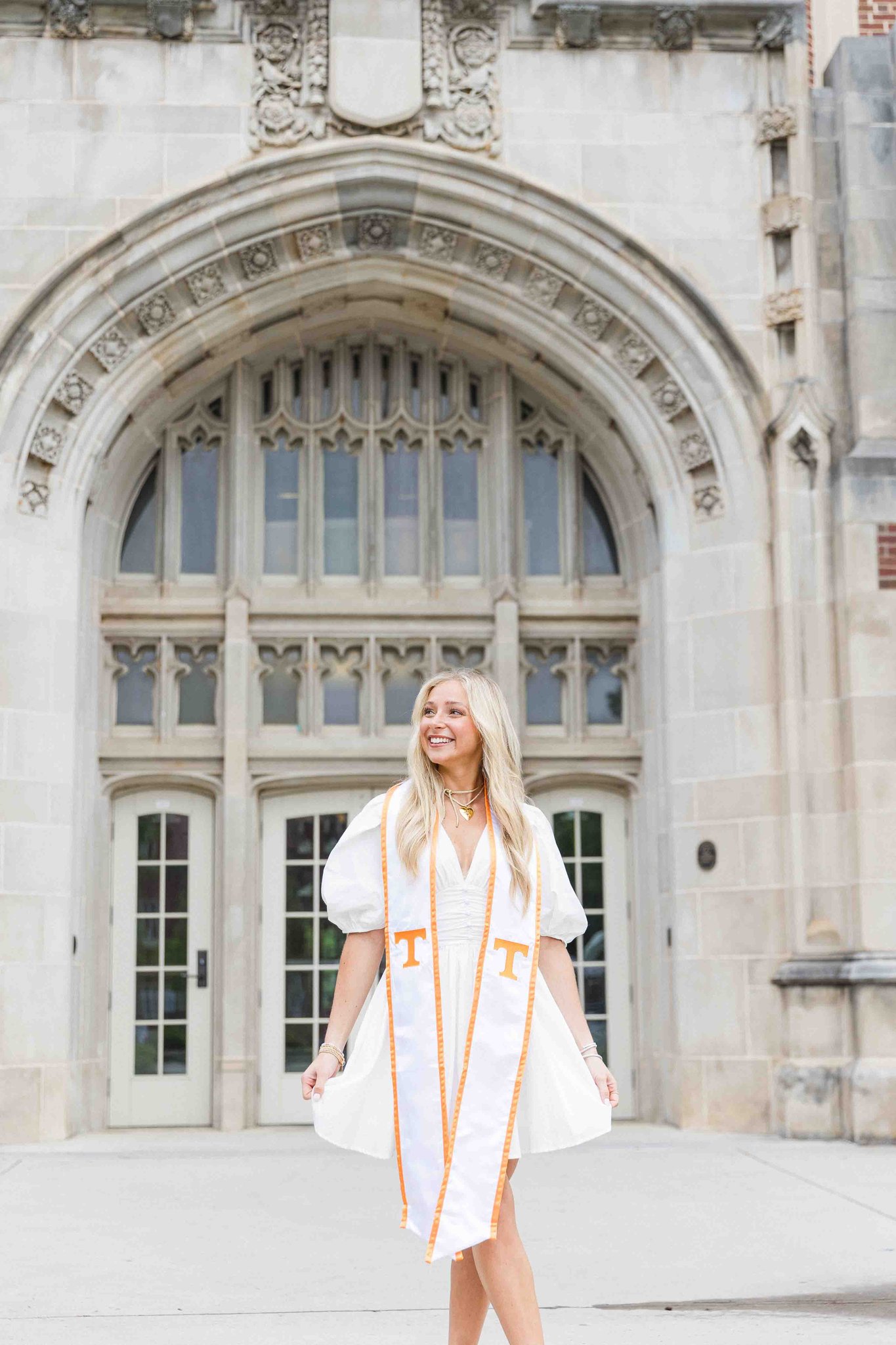 A woman in a white dress smiles while holding her white dress for her utk graduation pictures