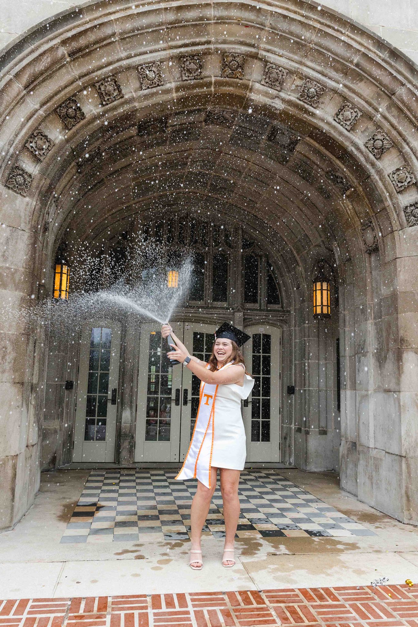 A happy grad pops a bottle of champagne at a building entrance during her utk graduation pictures