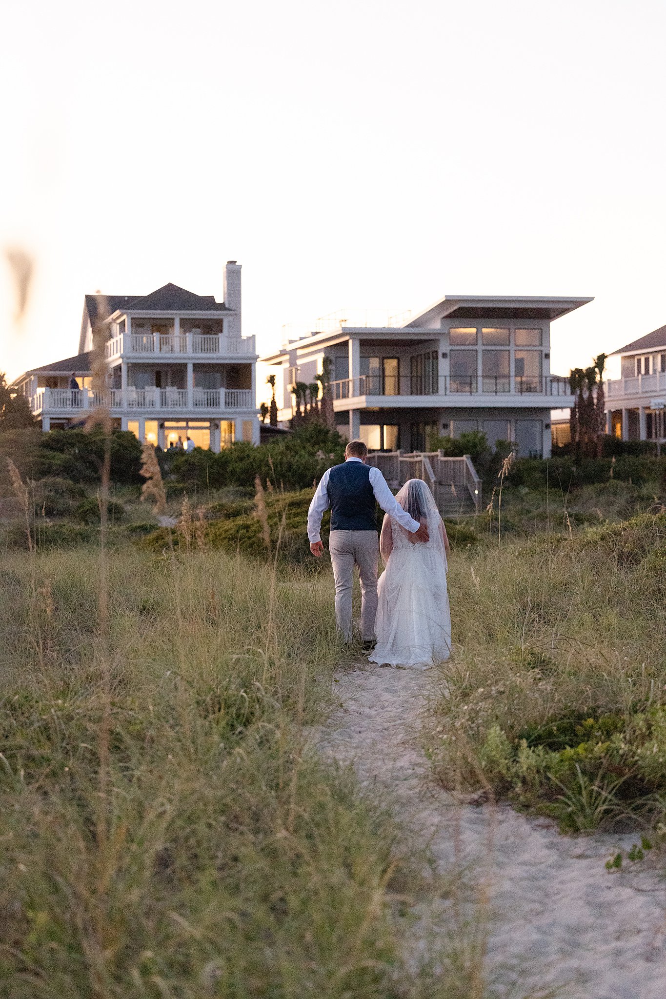 Newlyweds walk up a beach dune path together towards a beach house during their wrightsville beach wedding and elopement