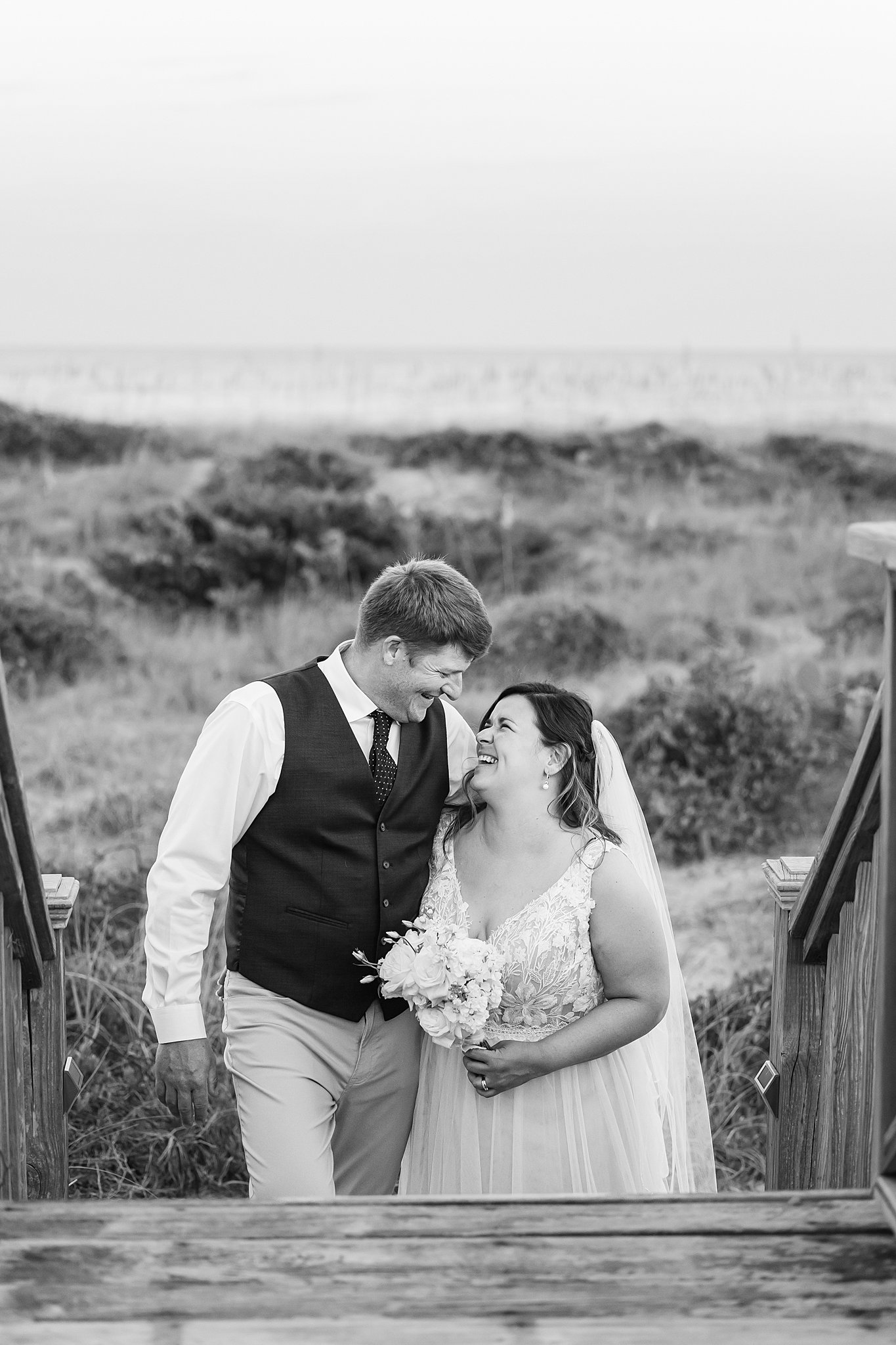 Newlyweds giggle at each other while walking up boardwalk stairs during their wrightsville beach wedding and elopement