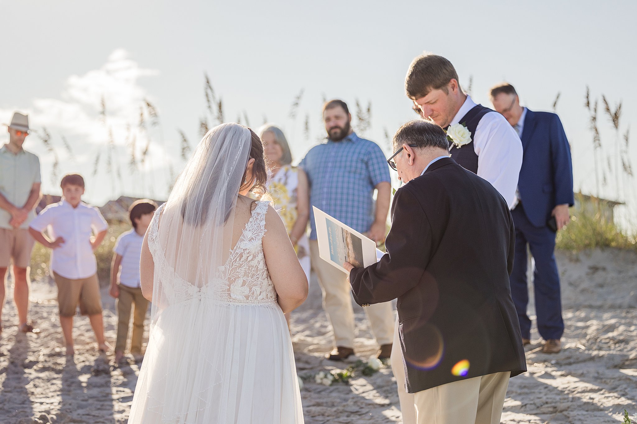 A view of a beach elopement during a prayer at sunset