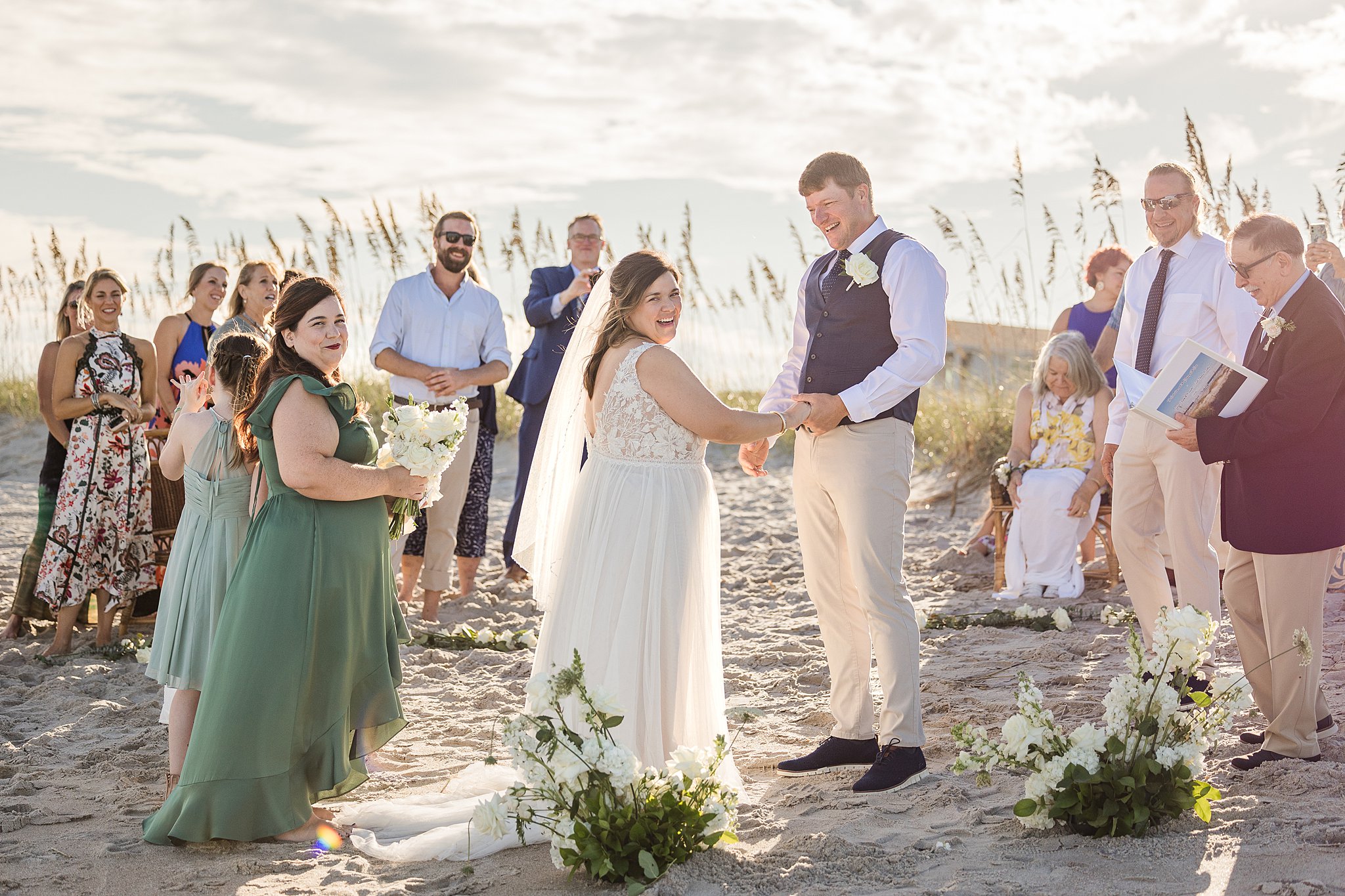 Newlyweds laugh while holding hands and standing on a beach during their wrightsville beach wedding and elopement