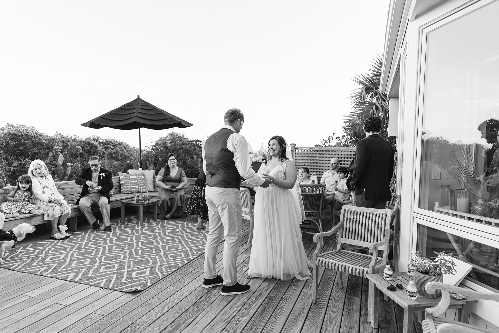 Newlyweds dance together on a beach deck with guests around them