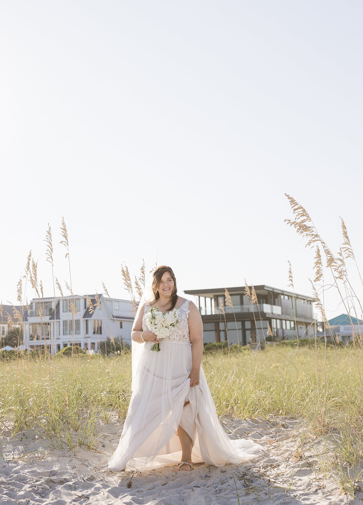 A bride holds her dress while walking on a beach at sunset during her wrightsville beach wedding and elopement