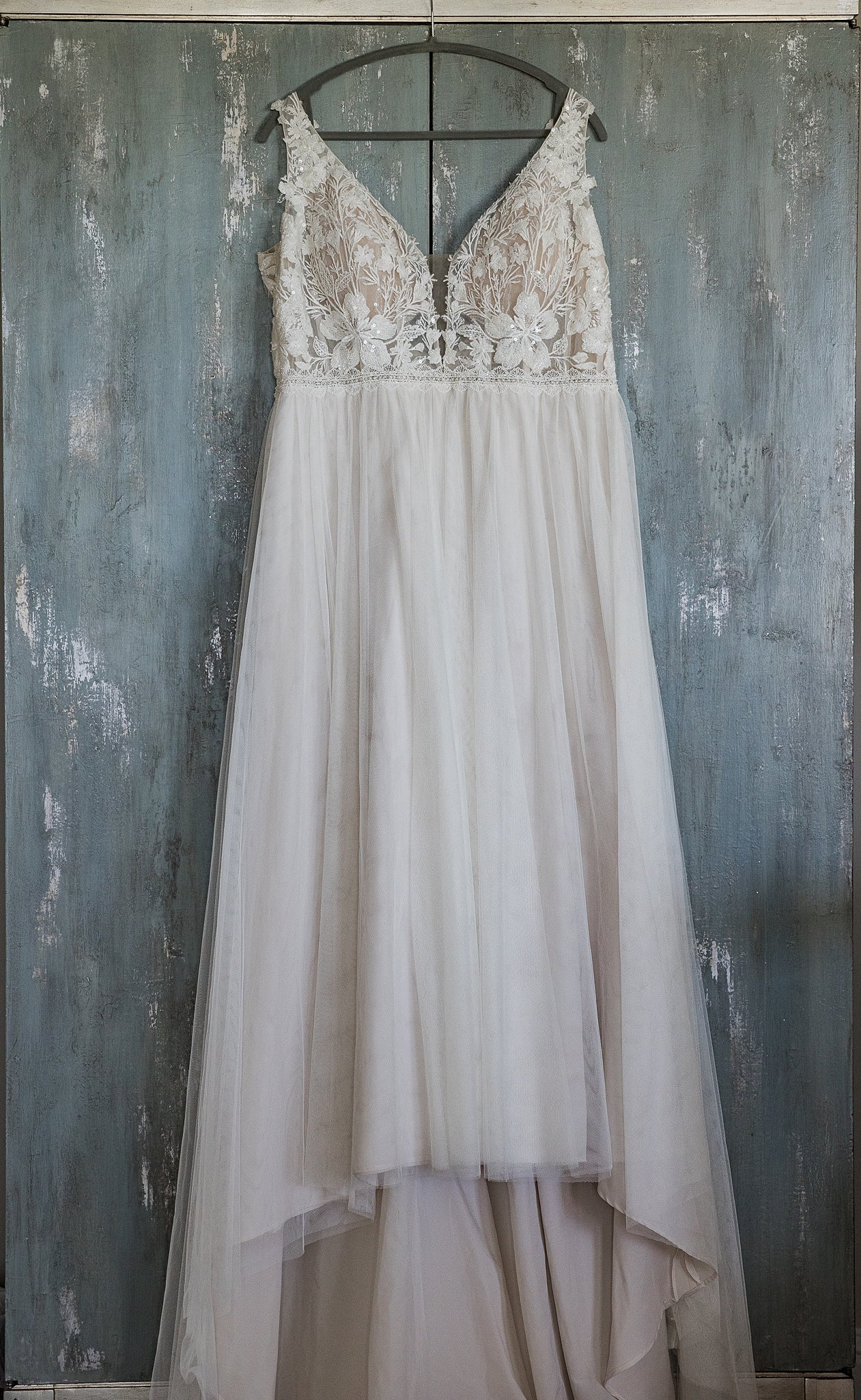 A white wedding dress with lace embroidered top hangs on a closet door