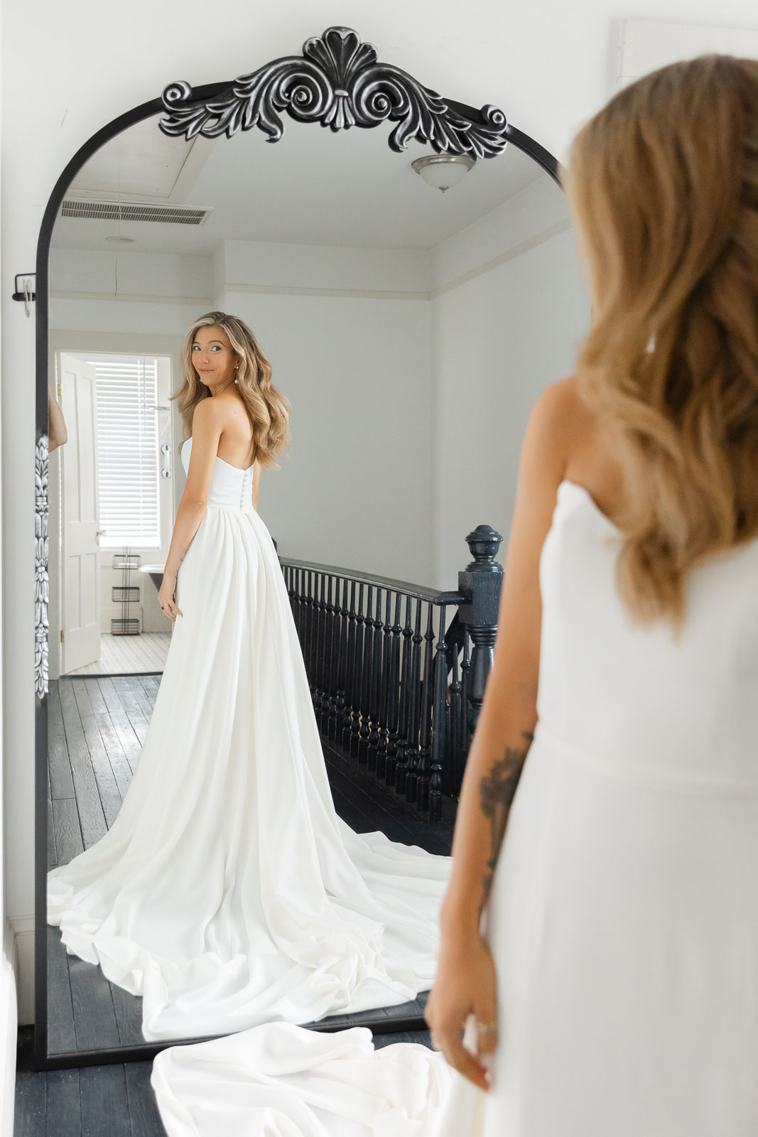 A bride looks over her shoulder to see her dress in a tall mirror before her Bakery 105 wedding