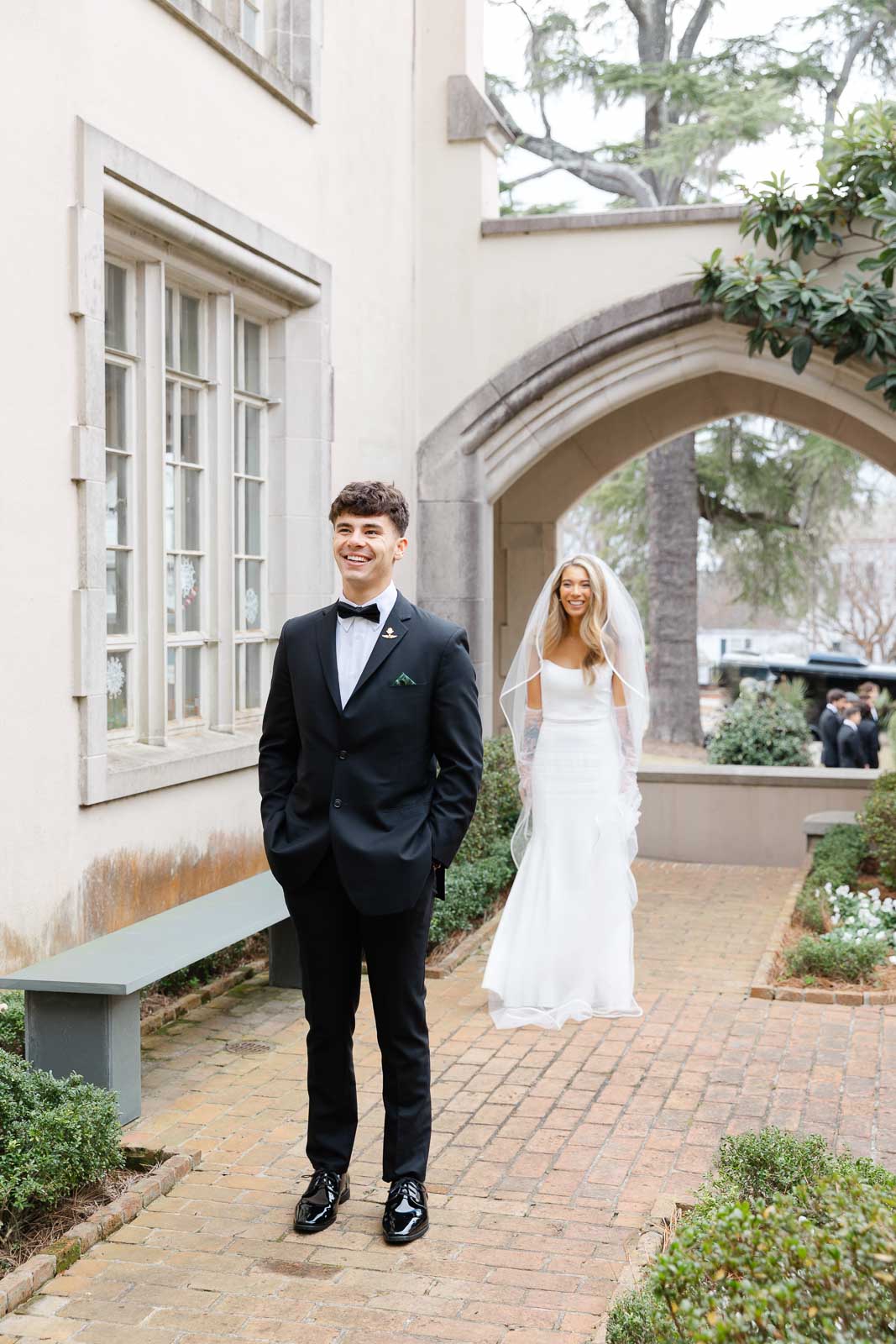 A groom smiles while waiting for his first look with his bride behind him at their Bakery 105 wedding