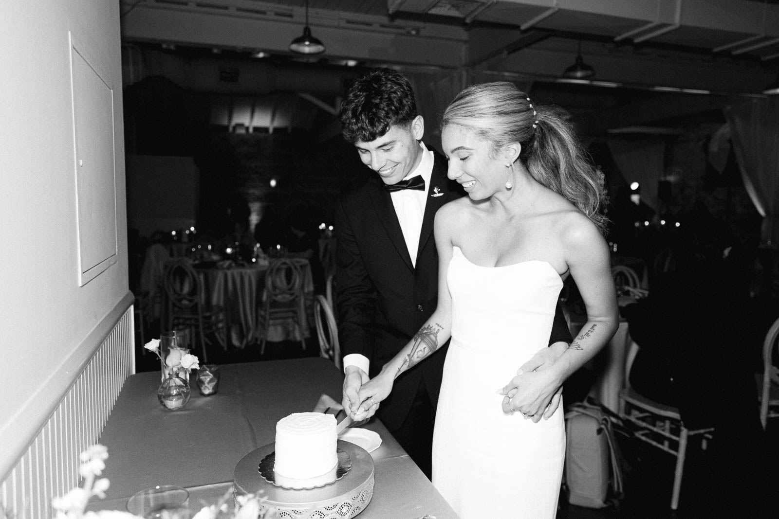 Newlyweds cut the cake while smiling and hugging in their reception