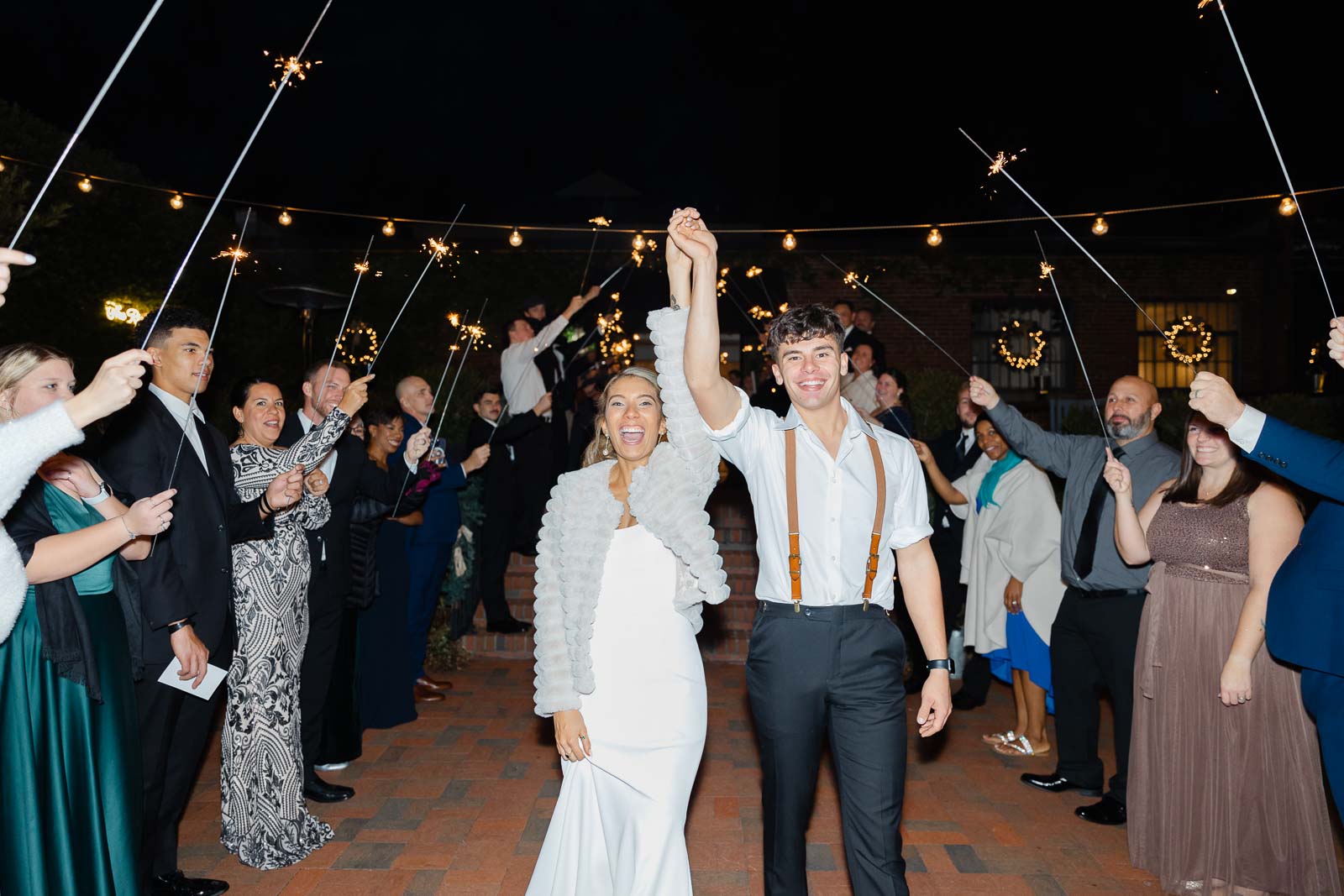 Newlyweds hold their hands up while walking under sparklers to exit their Bakery 105 wedding reception