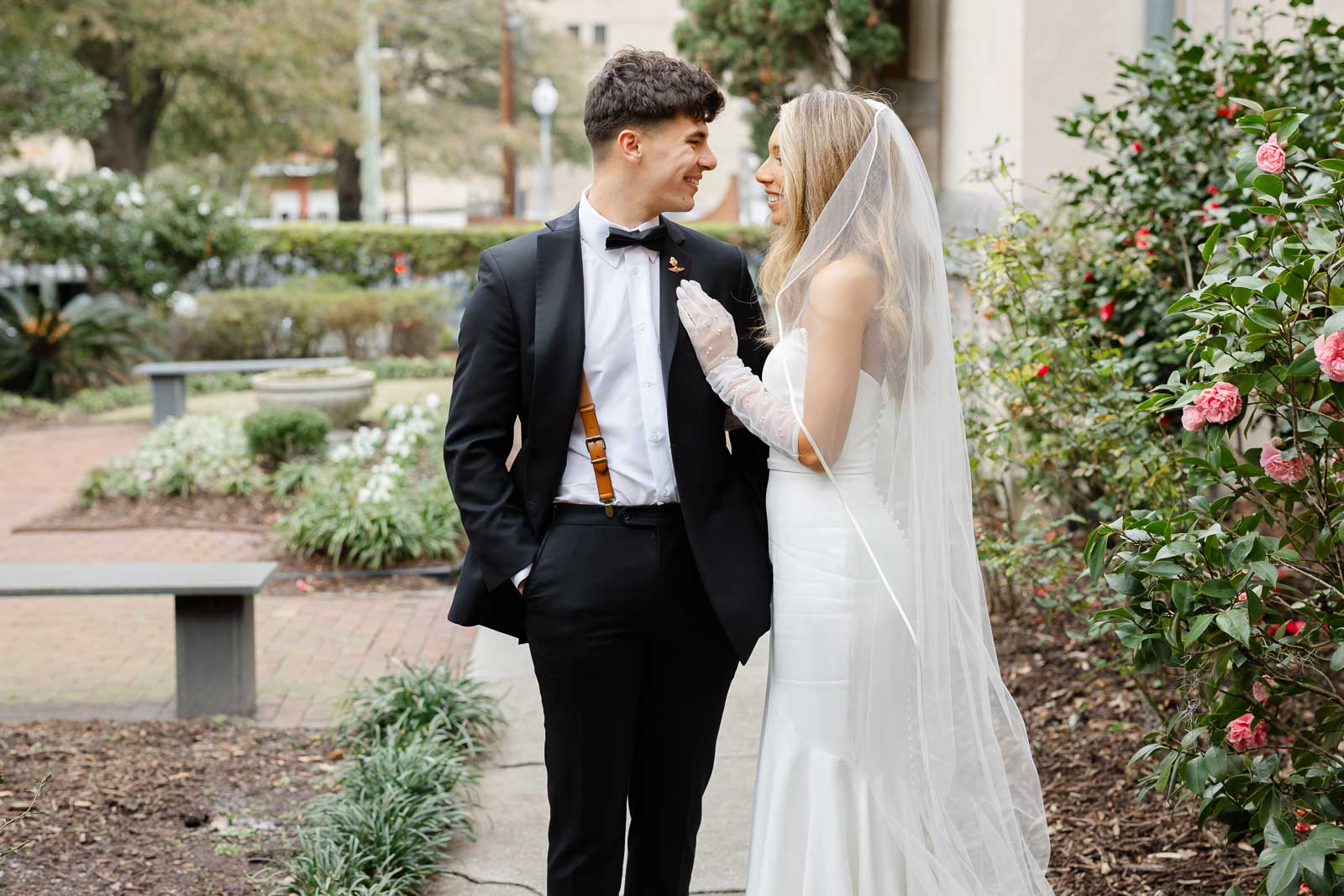 A bride hangs onto her groom while they walk through a rose garden during their Bakery 105 wedding