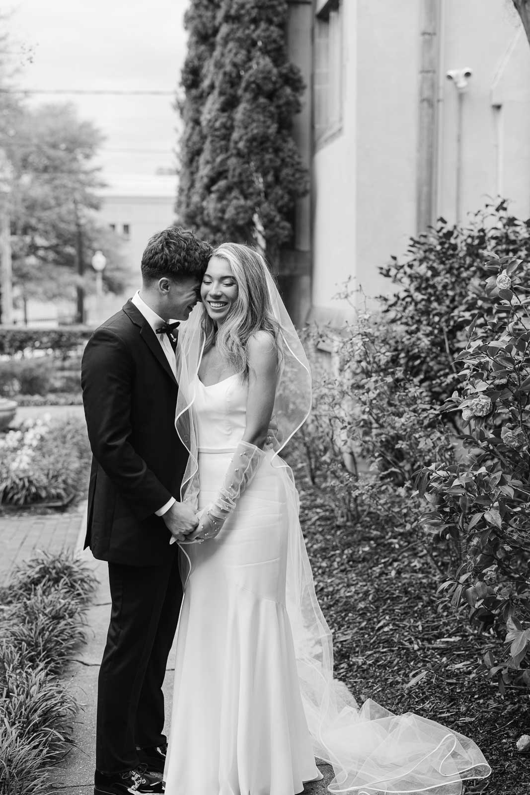 Newlyweds snuggle and giggle while standing in a garden during their Bakery 105 wedding