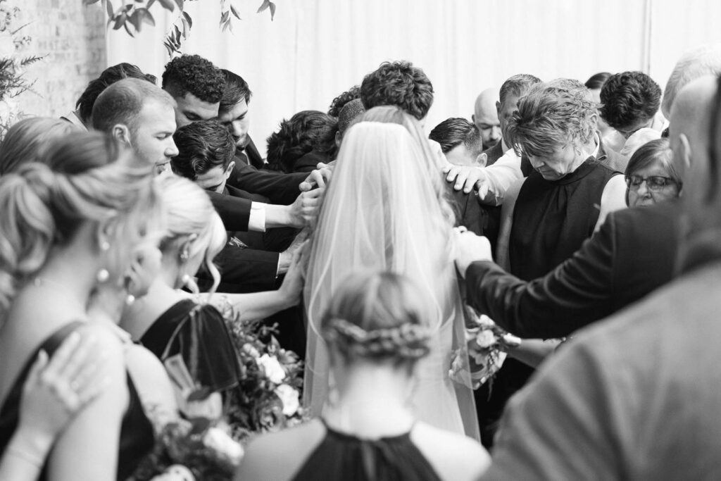 Newlyweds stand while their guests lay hands on them in prayer during their wedding ceremony